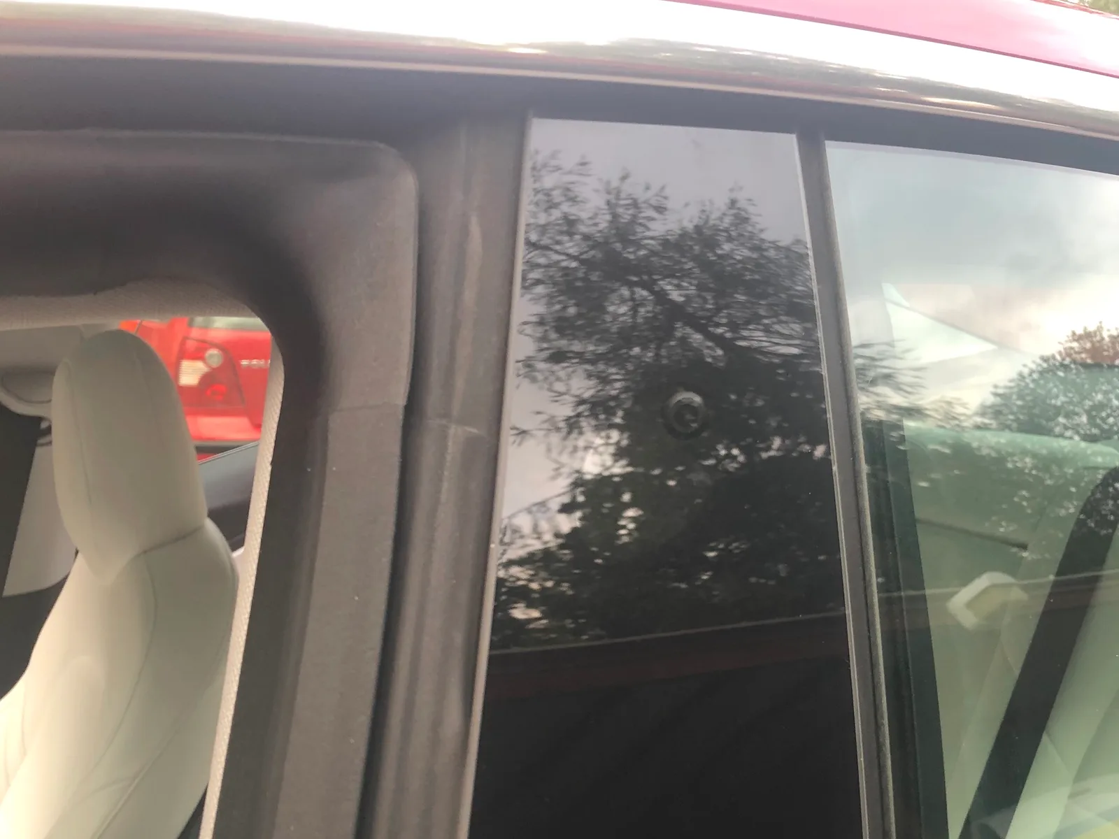 Den sorte stolpe mellem fordør og bagdør på en rød Tesla Model 3, med sidekameraet som en lille rund knap midt på panelet