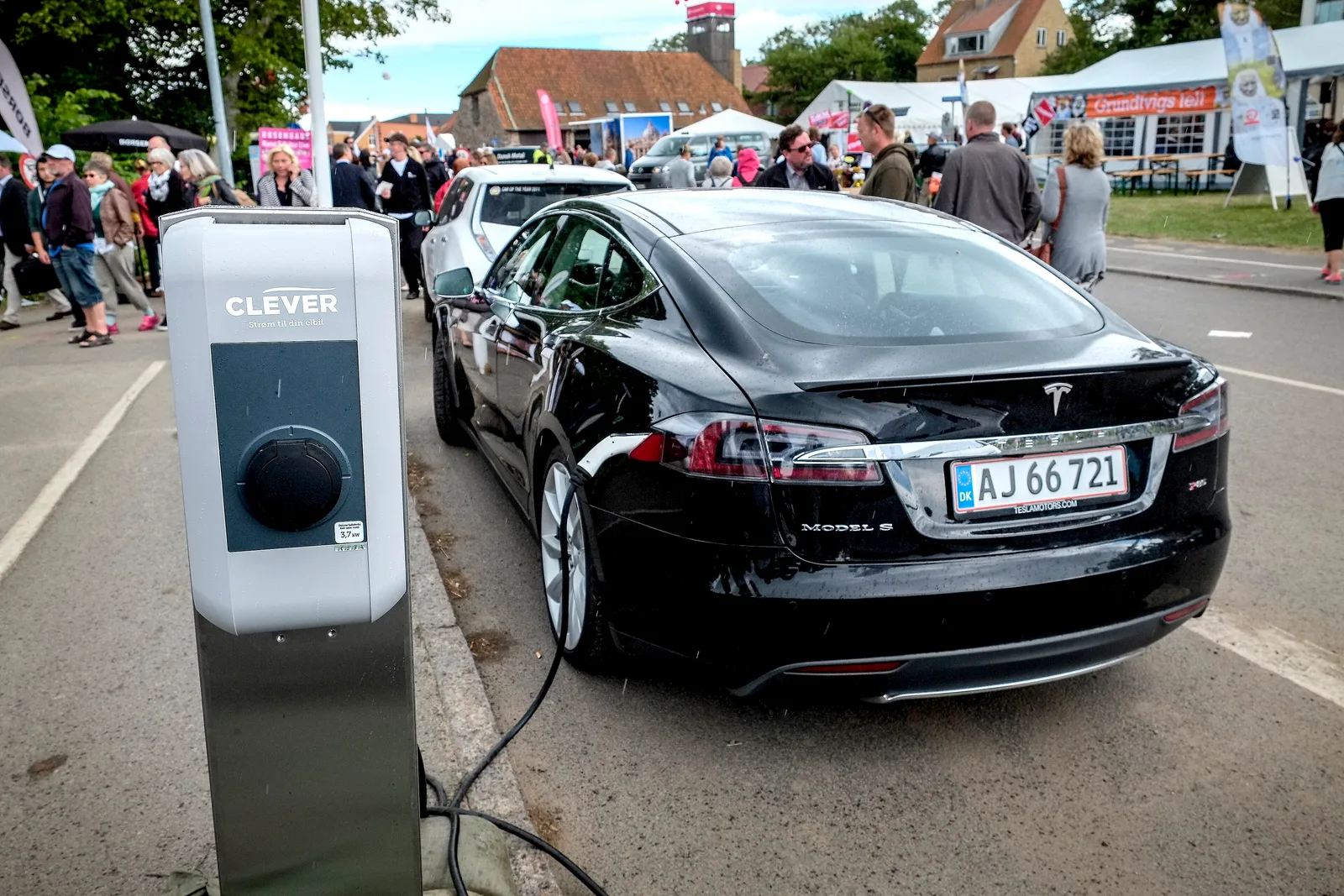 Sort Tesla Model S til opladning ved en dansk CLEVER-stander med ladekablet trukket hen over asfalten