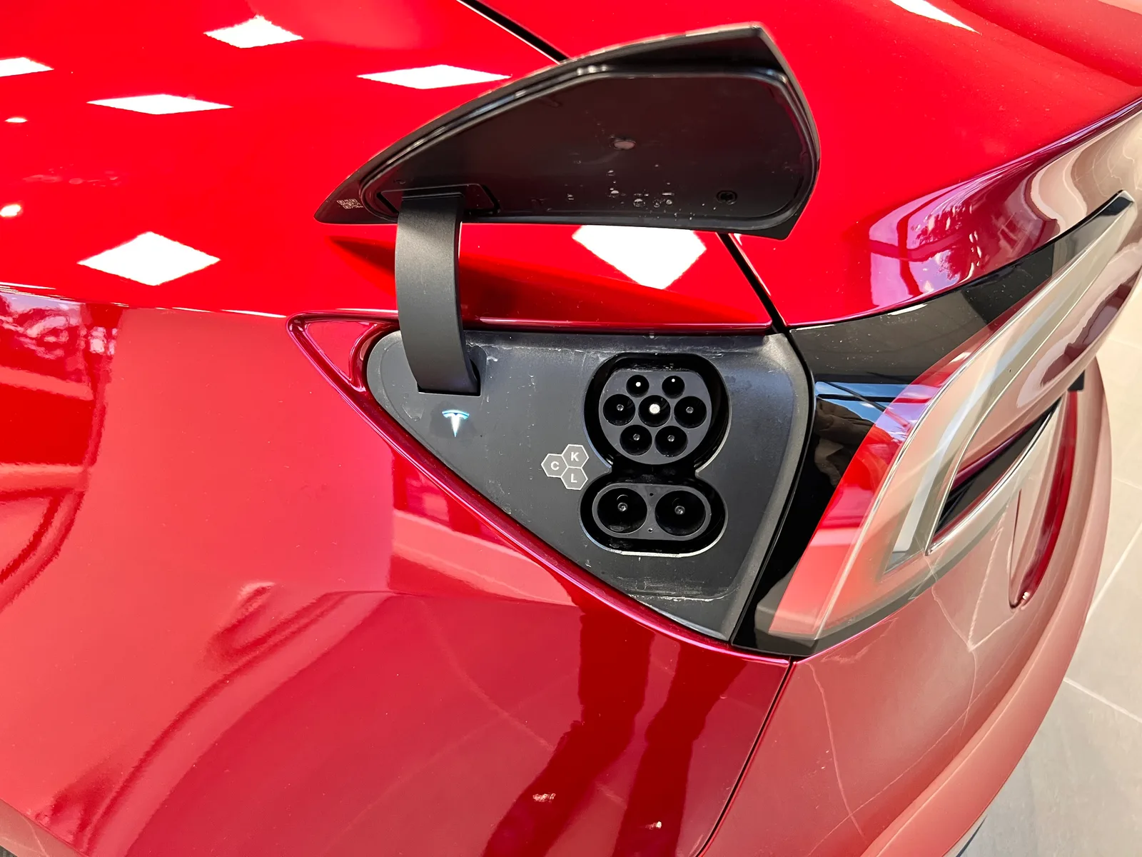 Åben ladeport på en rød Tesla Model 3 Highland med europæisk CCS Combo 2-stik. Lugen står op, og statuslyset lyser ved siden af stikket.