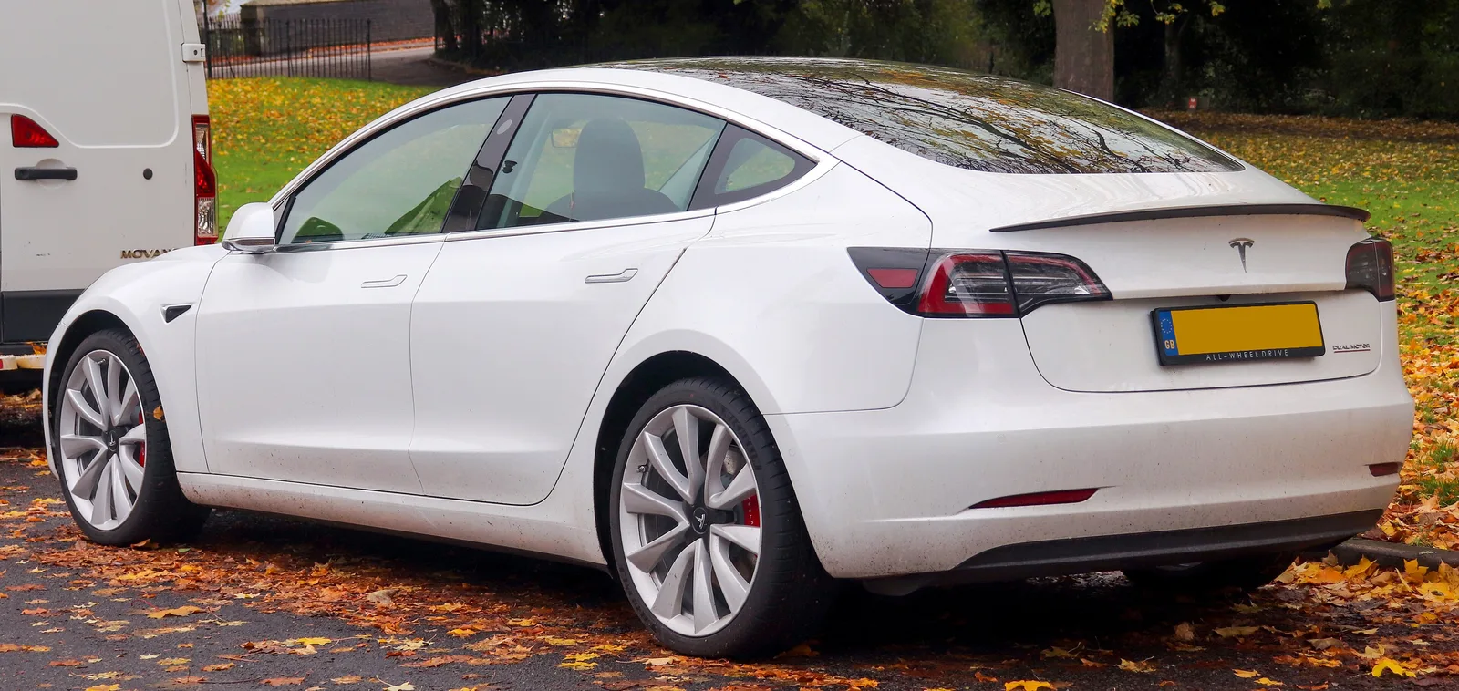 Hvid Tesla Model 3 fra 2019 set skråt bagfra i efterårsløv ved en park