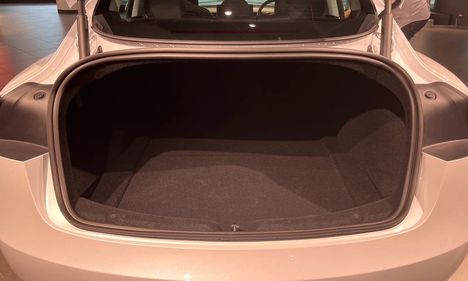 Det tomme bagagerum i en hvid Tesla Model 3 set lige bagfra med låget åbnet, bilen står i et udstillingslokale.
