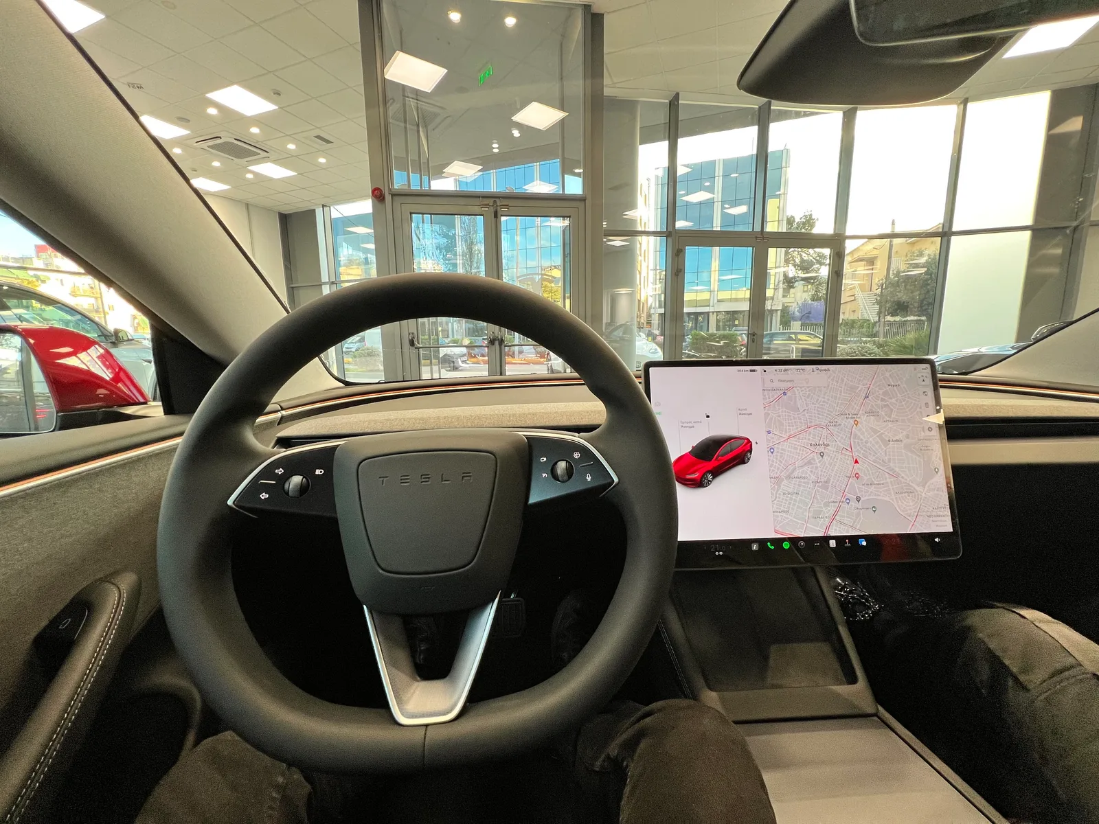 Førerpladsen i en Model 3 med skærmen tændt: bilen til venstre, kort til højre og appbjælken langs skærmens nederste kant