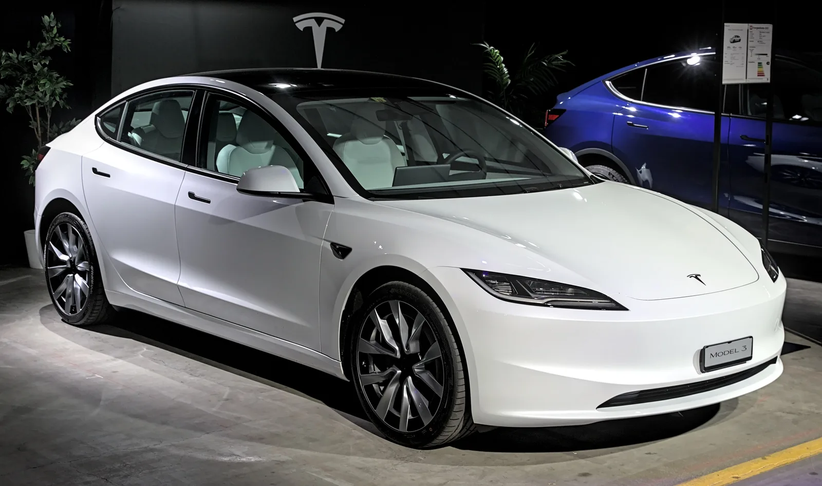 Hvid Model 3 Highland set skråt forfra i et mørkt udstillingslokale med de smalle forlygter tændt