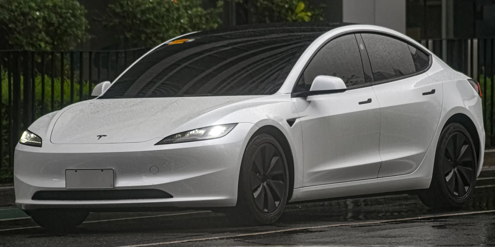 Hvid Model 3 Highland set skråt forfra i regnvejr med vand på lakken og forlygterne tændt