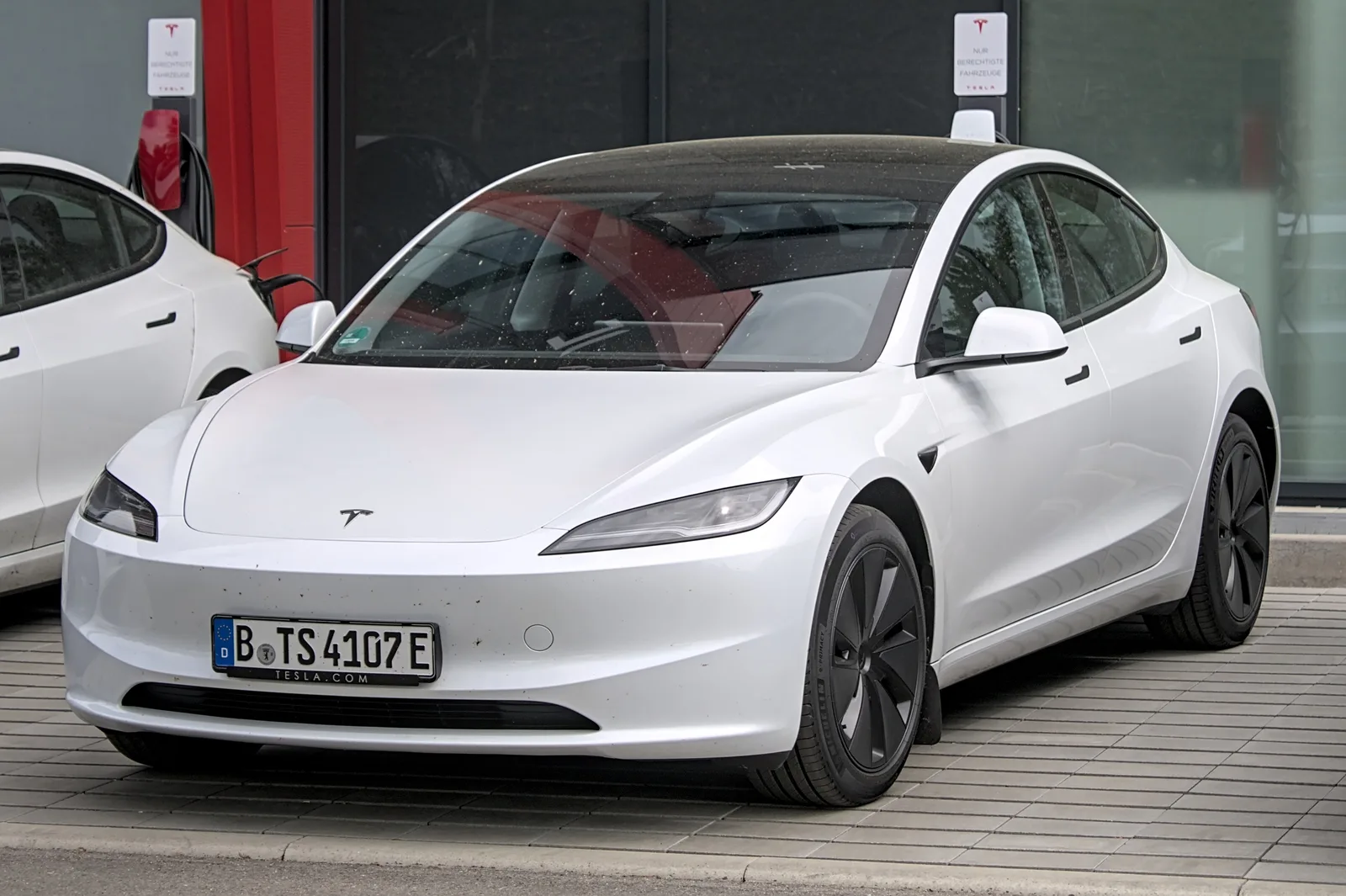Hvid Tesla Model 3 parkeret foran et Tesla Center med ladestandere langs facaden