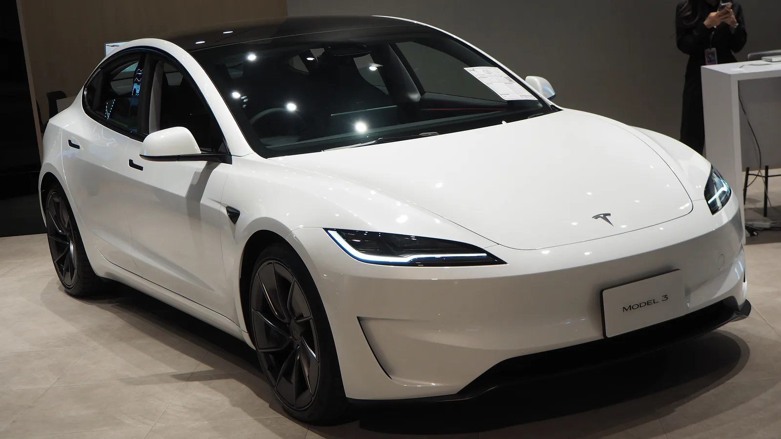 Hvid Tesla Model 3 Performance set skråt forfra i et lyst showroom med prisseddel i forruden og mørke sportsfælge