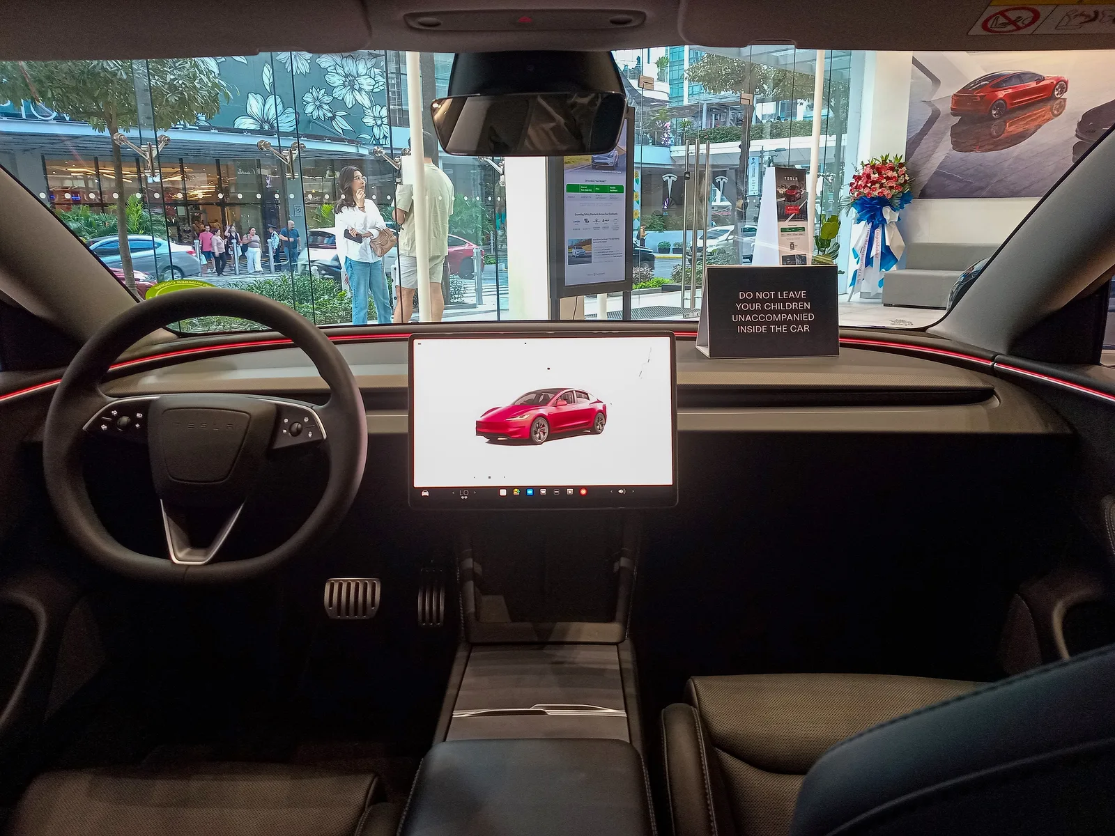 Kabinen i en Tesla Model 3 Performance set fra bagsædet, med rattet med rullehjul, den vandrette skærm og rødt lys langs instrumentbrættet