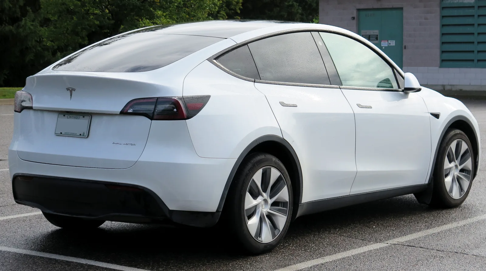 Hvid Tesla Model Y af den ældre udgave set skråt bagfra på en parkeringsplads i regnvejr