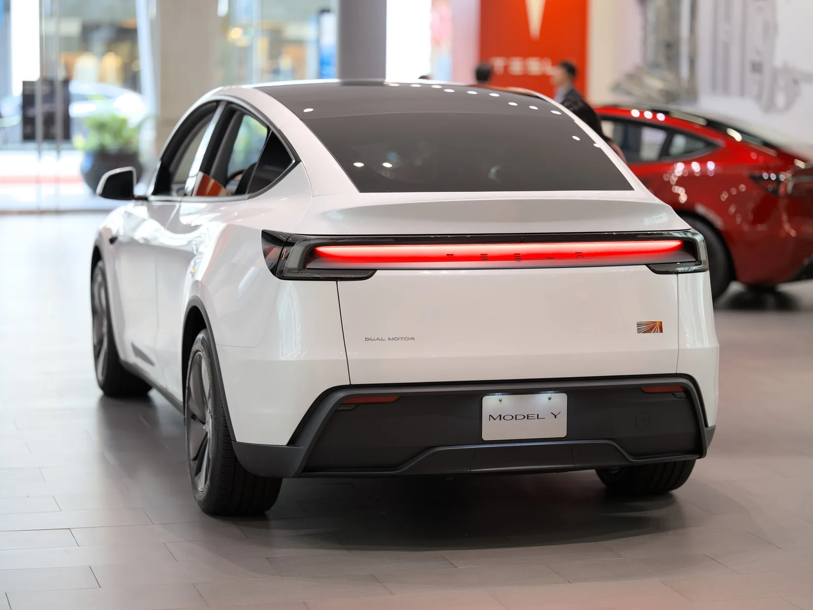 Hvid Tesla Model Y af 2025-udgaven set skråt bagfra i en Tesla-butik med den gennemgående røde lysstribe tændt
