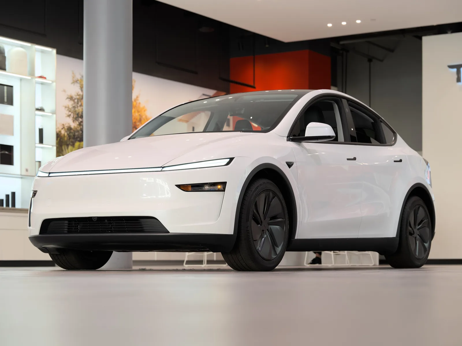 Hvid Tesla Model Y af 2025-udgaven set skråt forfra i lav kameravinkel i en Tesla-butik, med den gennemgående lysstribe tændt