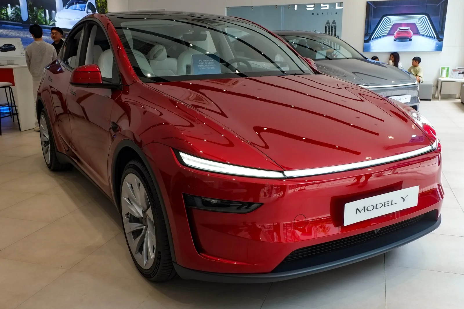 Rød Tesla Model Y af 2025-udgaven set skråt forfra i en Tesla-butik, med lyst interiør gennem ruderne og en grå Model Y bag den