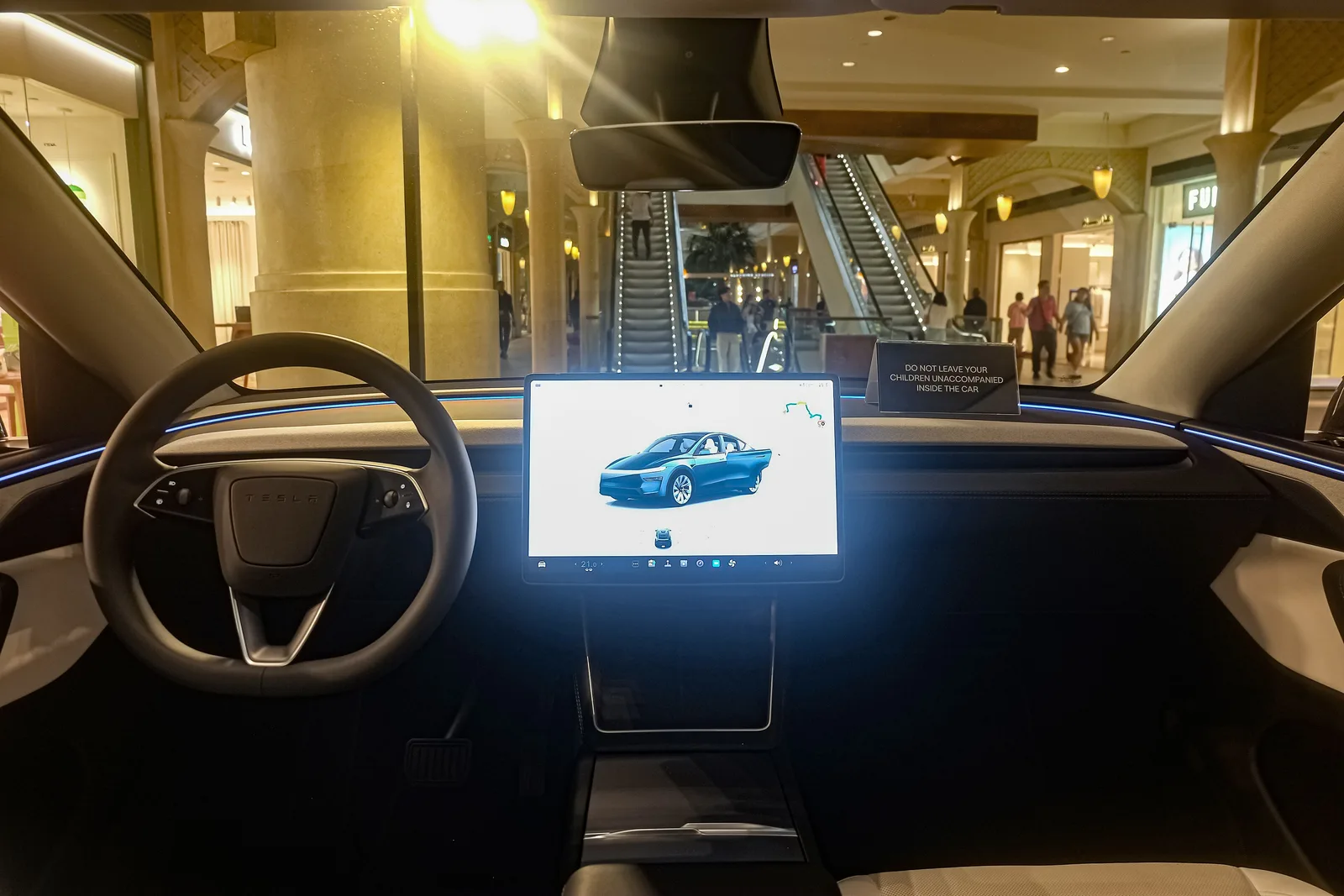 Instrumentbrættet i en Tesla Model Y set midt fra, med rat, den vandrette skærm og det blå ambientlys ud til begge sider