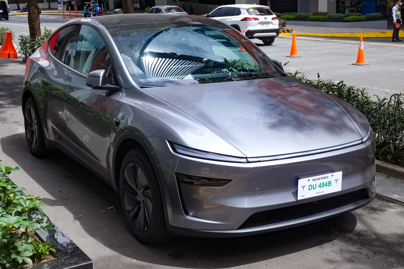 Grå Tesla Model Y af den nye udgave set skråt forfra parkeret ved et fortov, med lysbjælken tværs over fronten