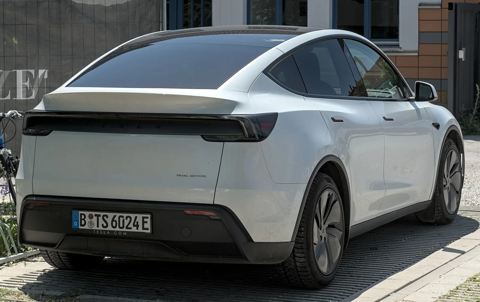 Hvid Tesla Model Y af den nye udgave set skråt bagfra på en flisebelagt plads, med det runde dæksel over trækhuset synligt nederst i kofangeren