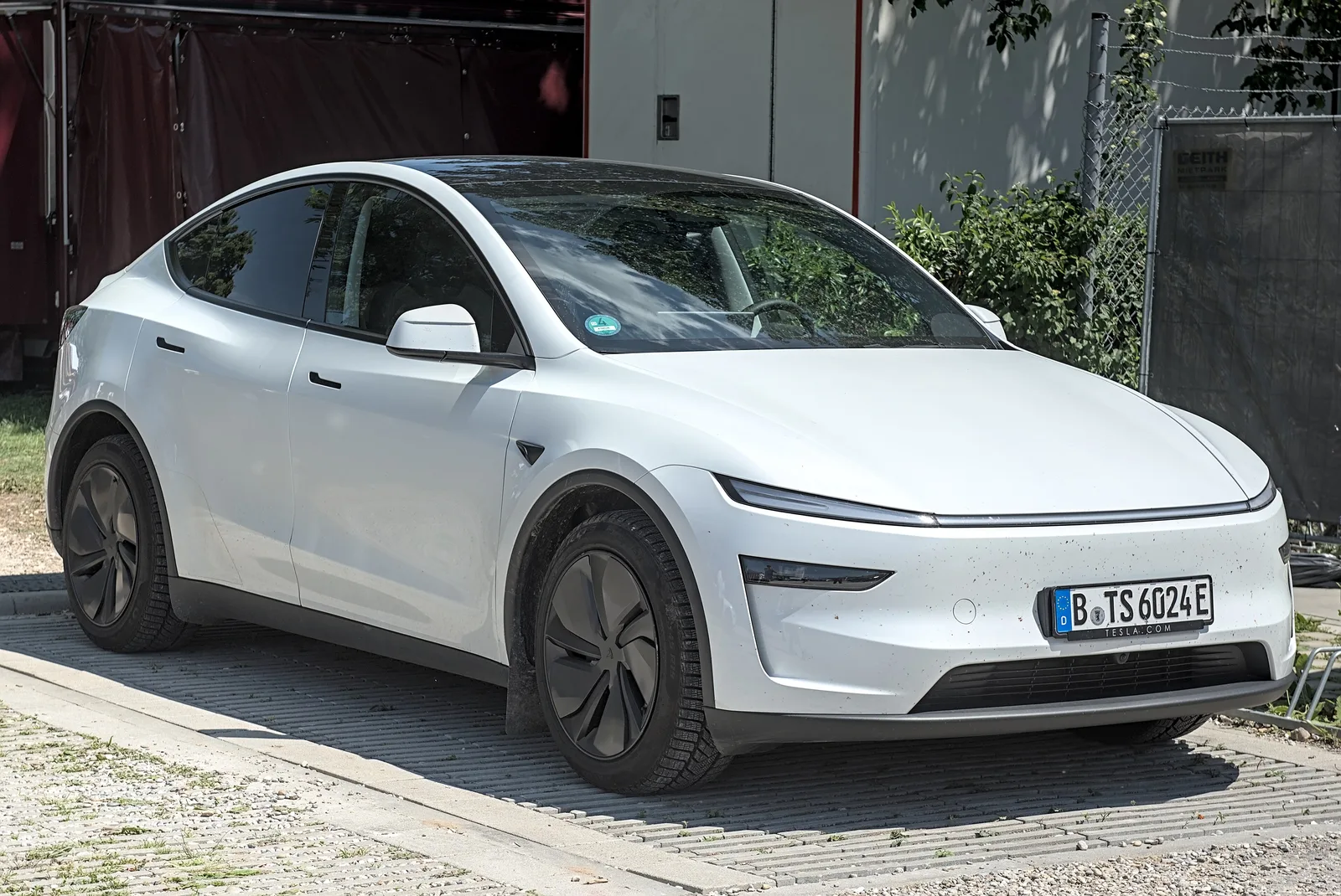 Hvid Tesla Model Y set skråt forfra på en flisebelagt plads med tysk demoplade fra Tesla Berlin