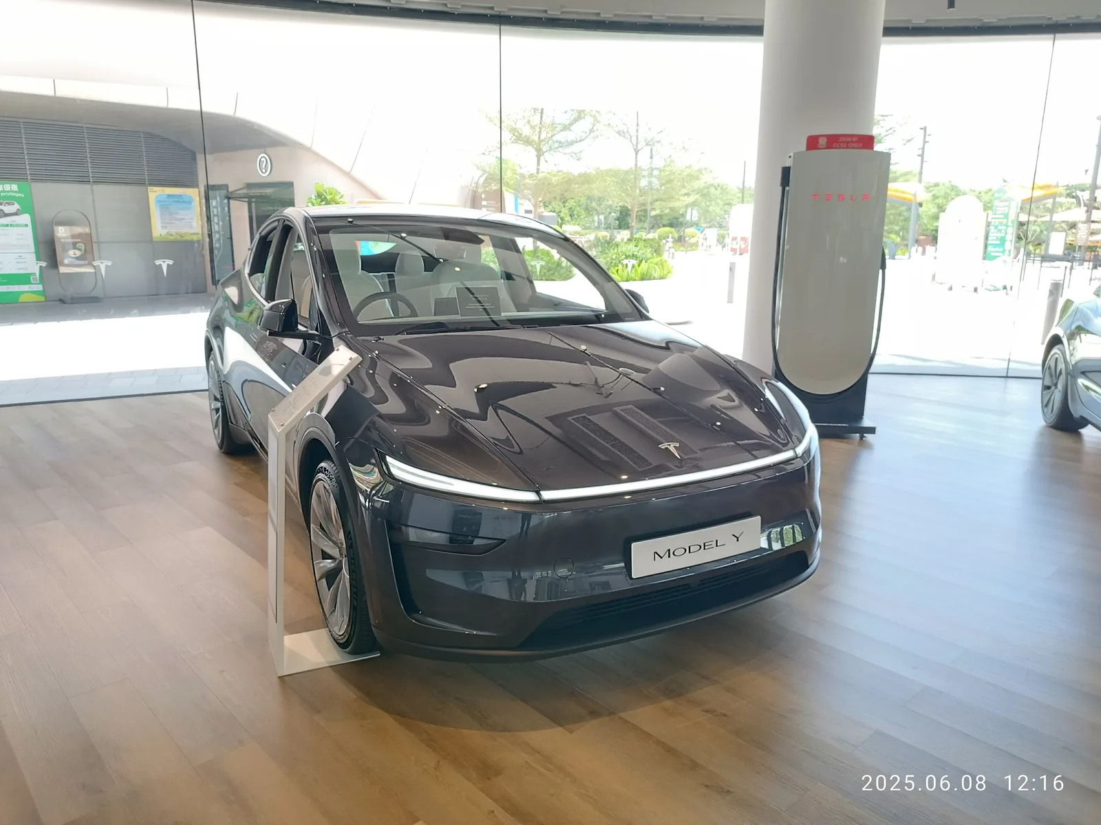 Mørkegrå Tesla Model Y udstillet i et lyst showroom med et Model Y-skilt foran og en Supercharger-stander ved siden af