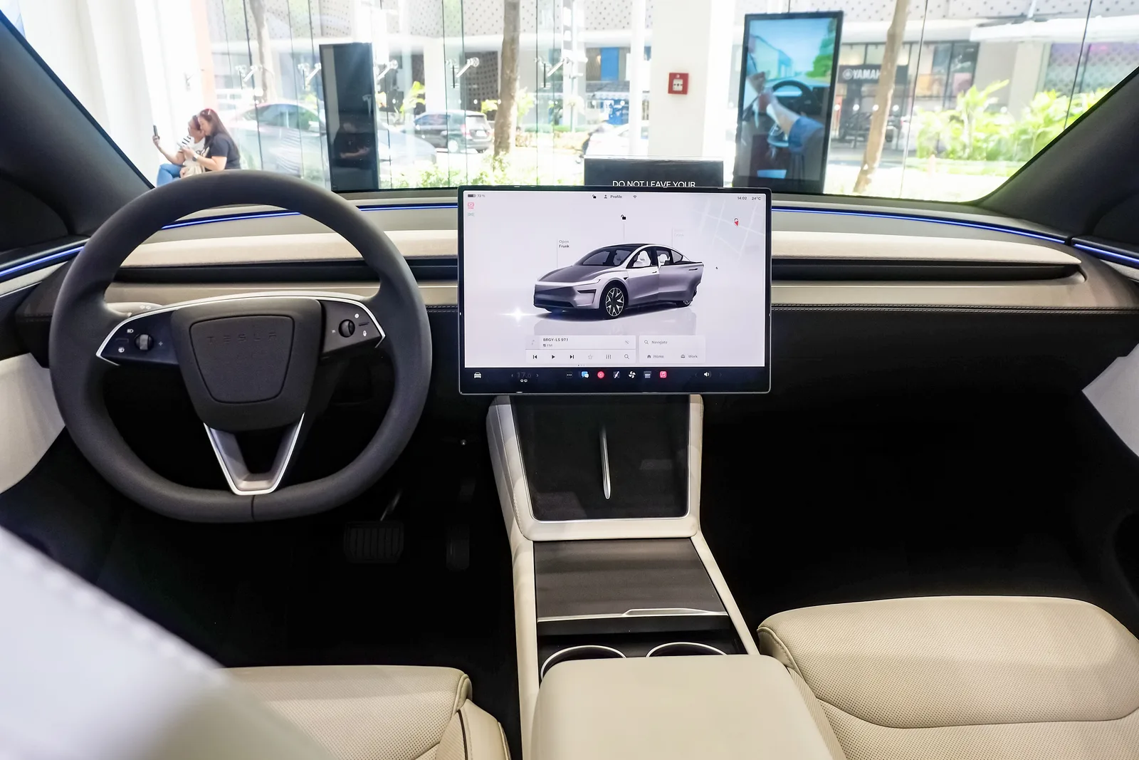 Førerpladsen i en ny Tesla med lyst interiør, rat med rullehjul og den vandrette skærm, hvor medieafspilleren ligger nederst under bilgengivelsen