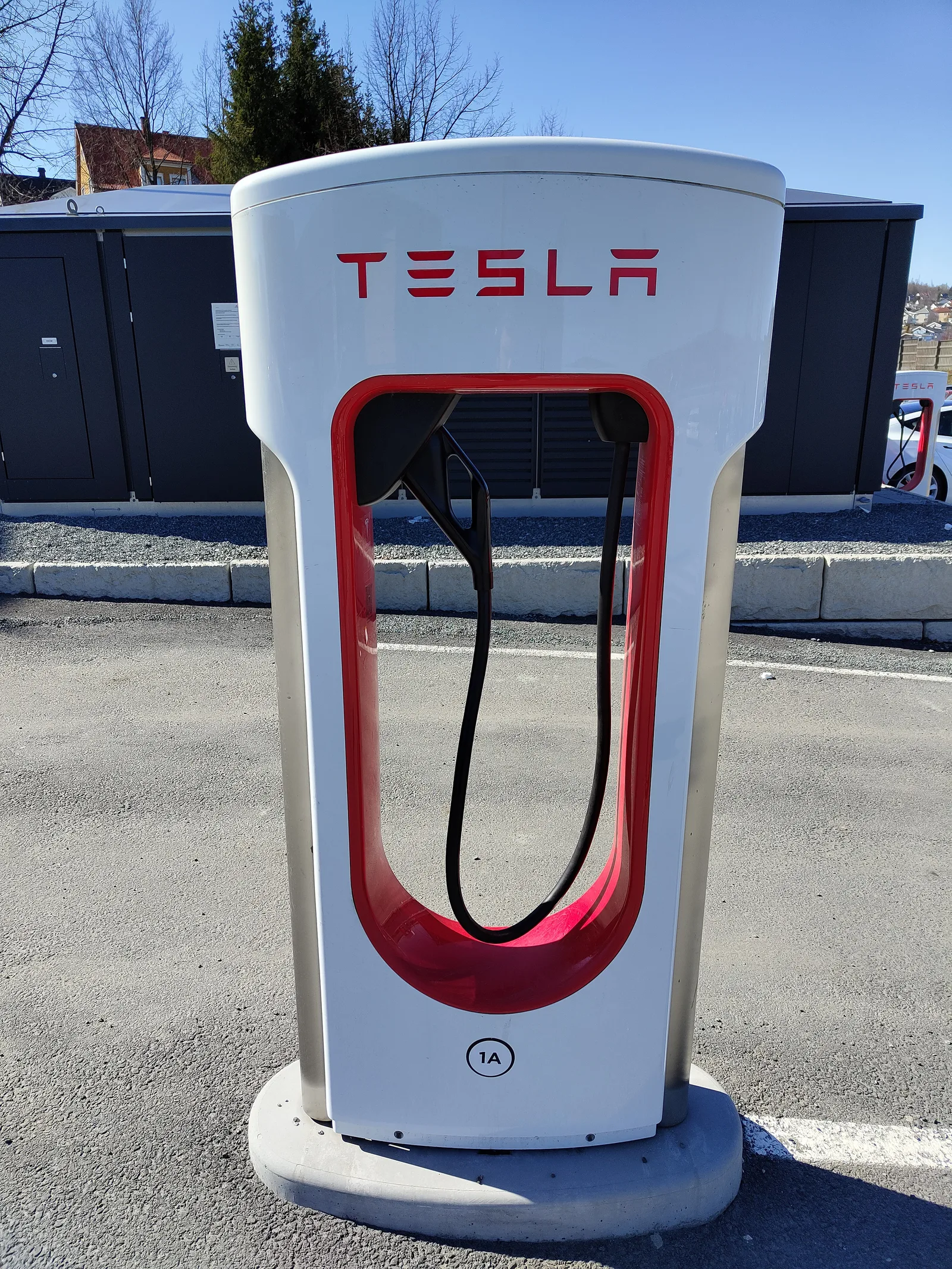 En Tesla Supercharger set lige forfra med ladekablet hængende i holderen