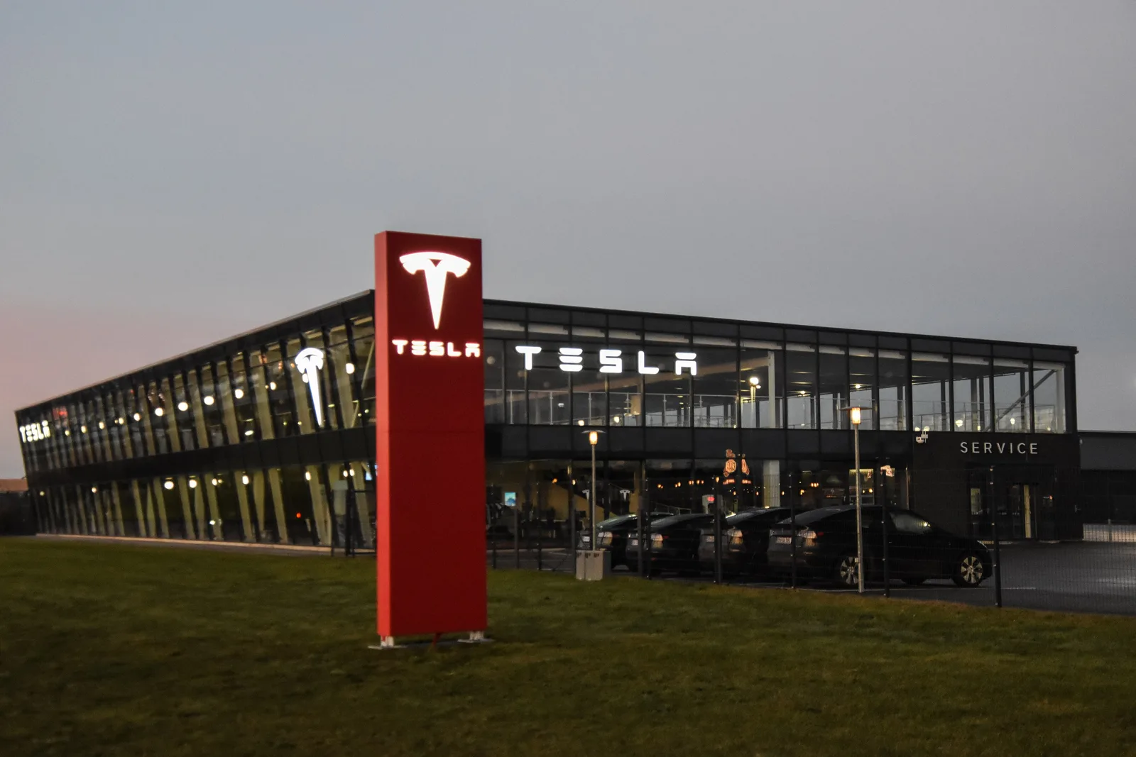 Et Tesla Center i tusmørke med oplyst facade, rødt Tesla-tårn foran og indgang mærket Service