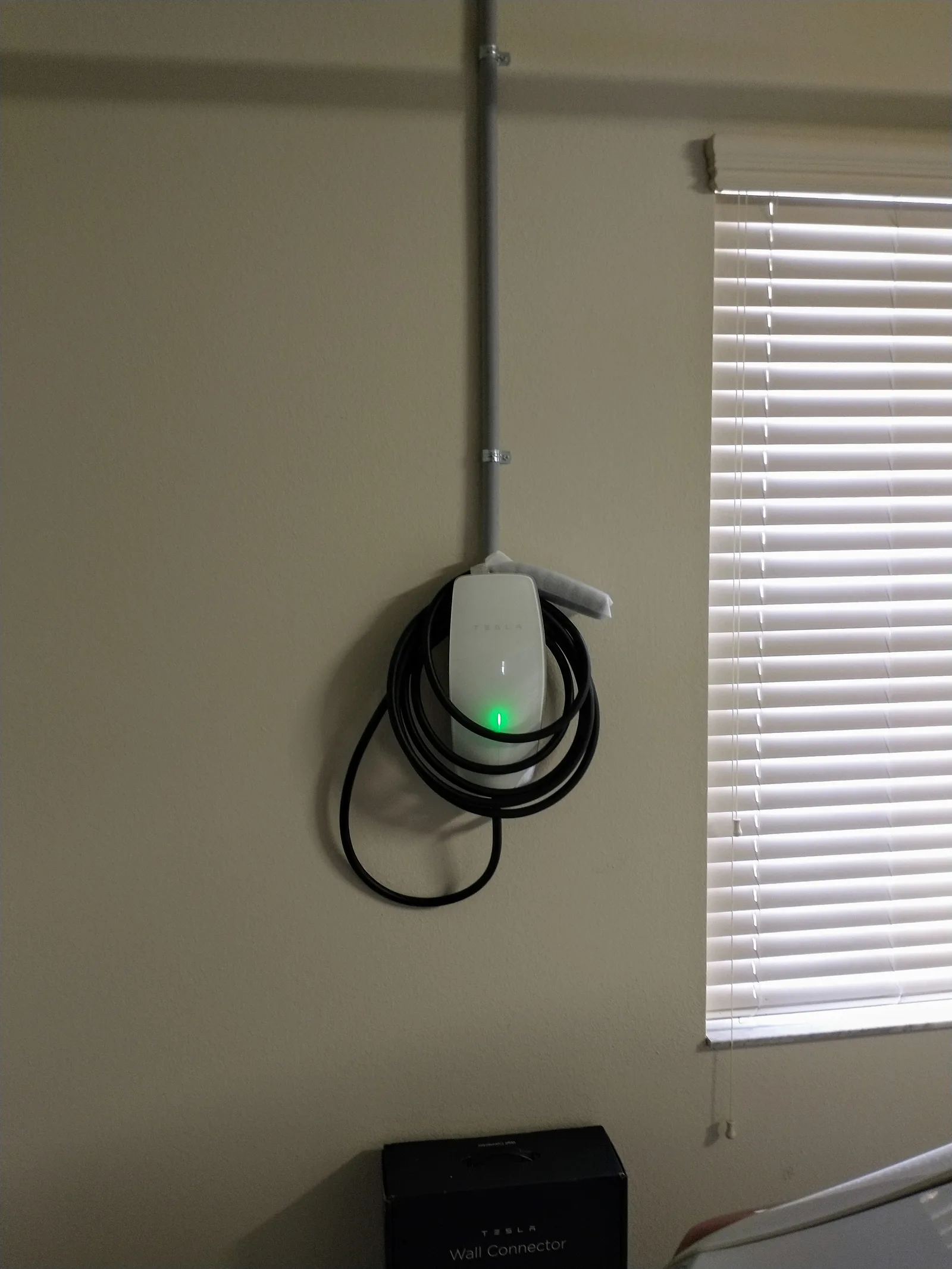 En Tesla Wall Connector monteret på en garagevæg med kablet rullet op om enheden og den grønne lampe tændt